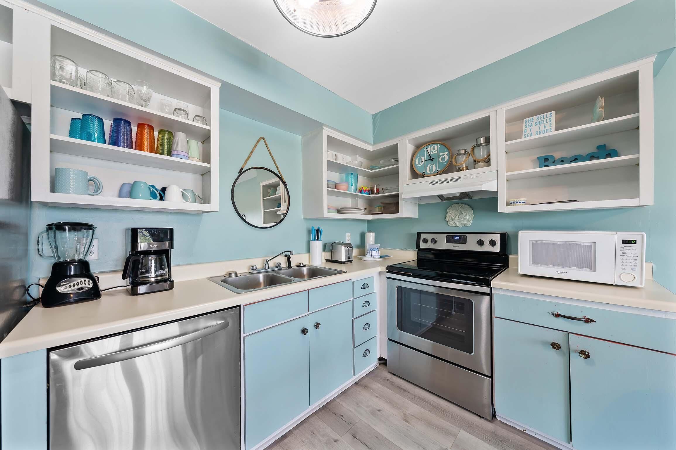 Una cocina con armarios azul claro, electrodomésticos de acero inoxidable y diverso menaje de cocina en estantes.