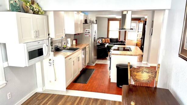 A compact kitchen with white cabinets, a built-in microwave, and a wooden dining table with a chair.