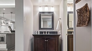 A modern bathroom with a dark wooden vanity, a large mirror, and a light fixture above the sink.
