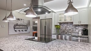 A modern kitchen with granite countertops, stainless steel appliances, pendant lighting, and a backsplash.