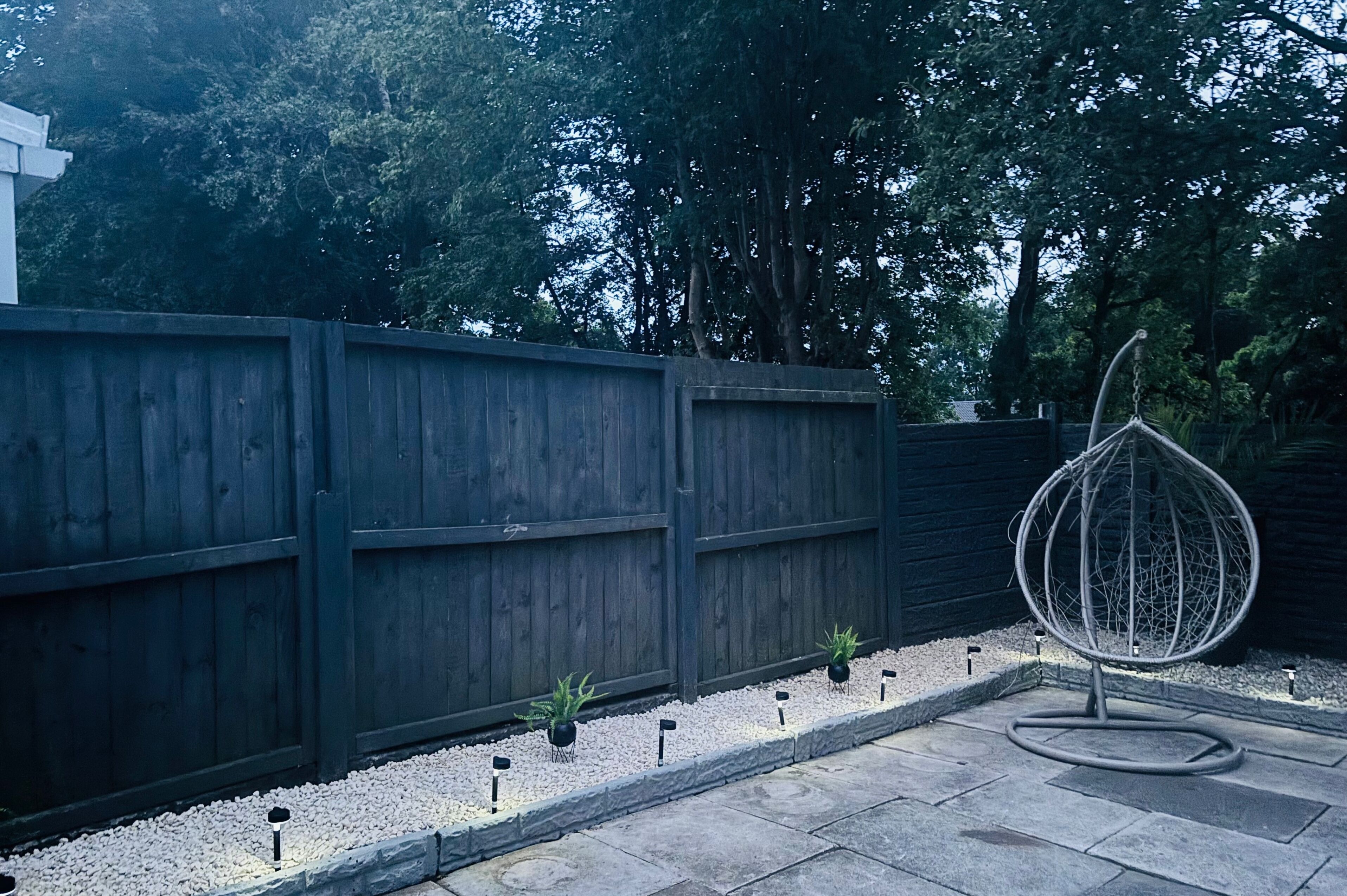 Une clôture en bois, une sculpture sphérique en métal et de petites plantes en pot dans un espace aménagé en jardin.
