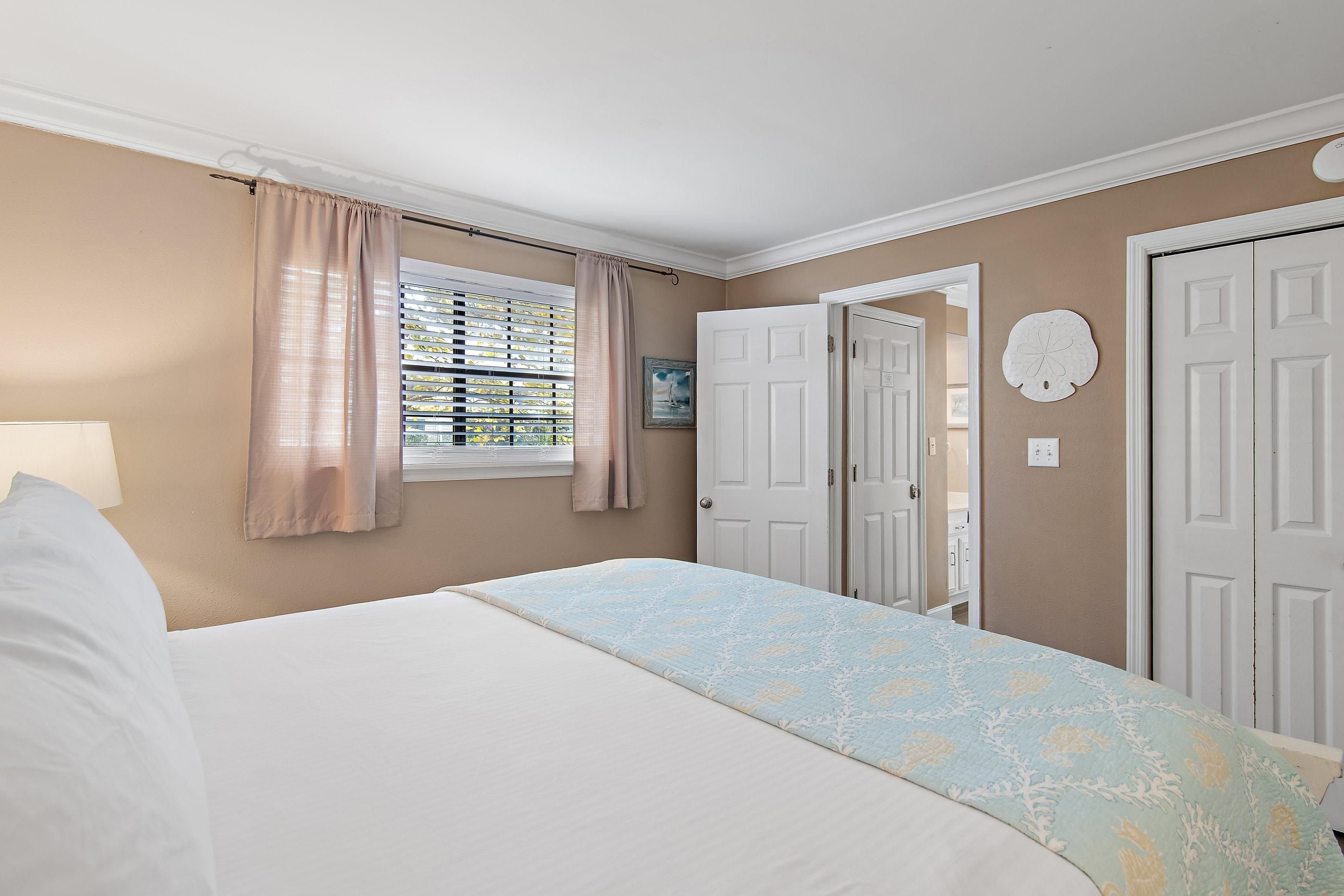 Une chambre à coucher avec un lit, une fenêtre avec des stores, une porte et un interrupteur fixé au mur.
