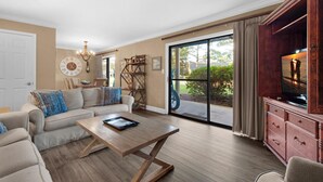 A spacious living room with a sofa, coffee table, and a television on a wooden cabinet. - Seascape 22a- Hello Sunshine (Miramar Beach)