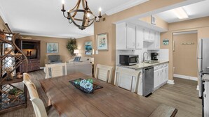A modern kitchen with white cabinets, a microwave, and a dishwasher. There is a dining area with a wooden table and chairs. - Seascape 22a- Hello Sunshine (Miramar Beach)