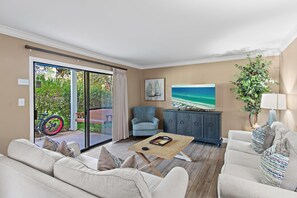 Ett vardagsrum med en soffa, en fåtölj, ett soffbord och en tavla som föreställer en strandvy.
