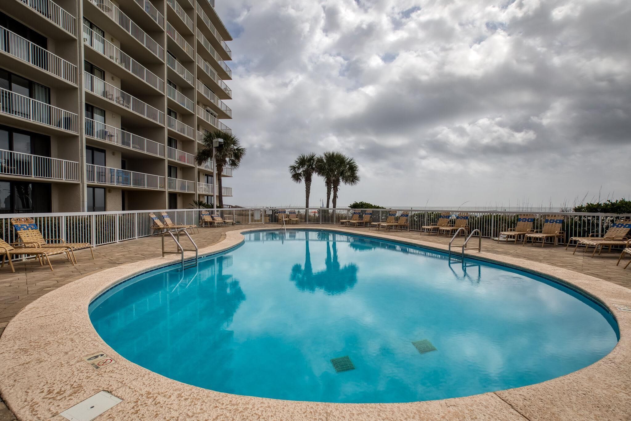 A swimming pool with lounge chairs and palm trees, surrounded by a high-rise building.