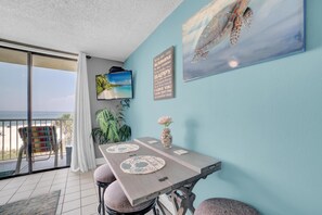 A dining area with a table, chairs, and a view of the beach. - Seaside Beach & Racquet 3305 (Orange Beach)