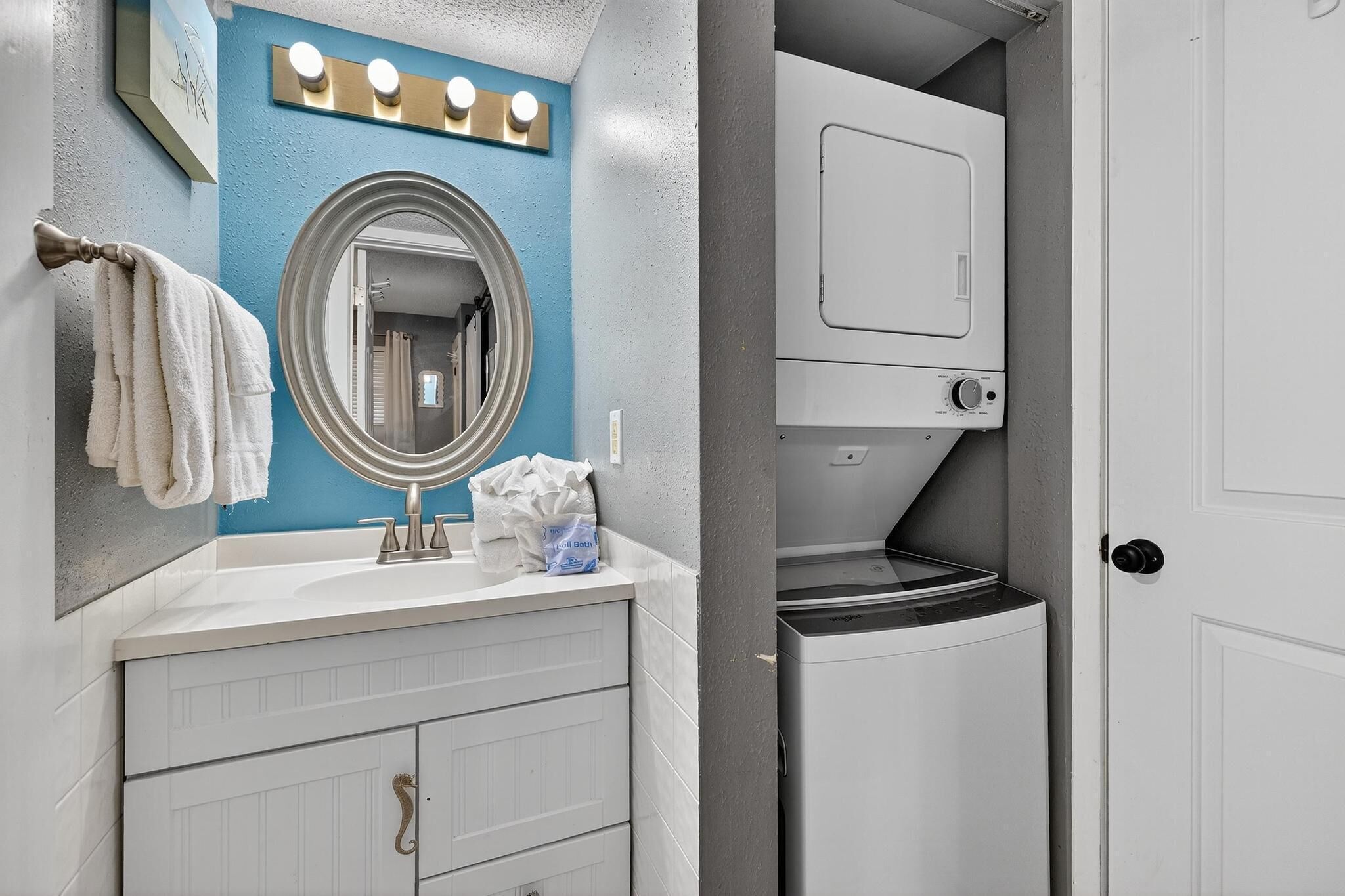 Une salle de bain avec un meuble-lavabo blanc, un miroir rond et un lave-linge encastré.