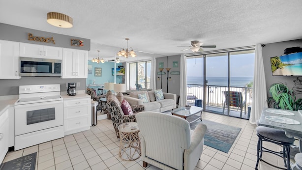 A spacious living area with a kitchen, a balcony with a view of the ocean, and a ceiling fan. - Seaside Beach & Racquet 3305 (Orange Beach)