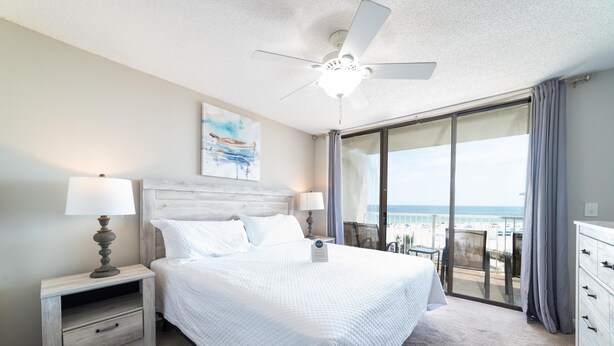 A hotel room with a large bed, two bedside lamps, a ceiling fan, a view of the ocean, and a balcony with a table and chairs. - Seaside Beach & Racquet 3401 (Orange Beach)