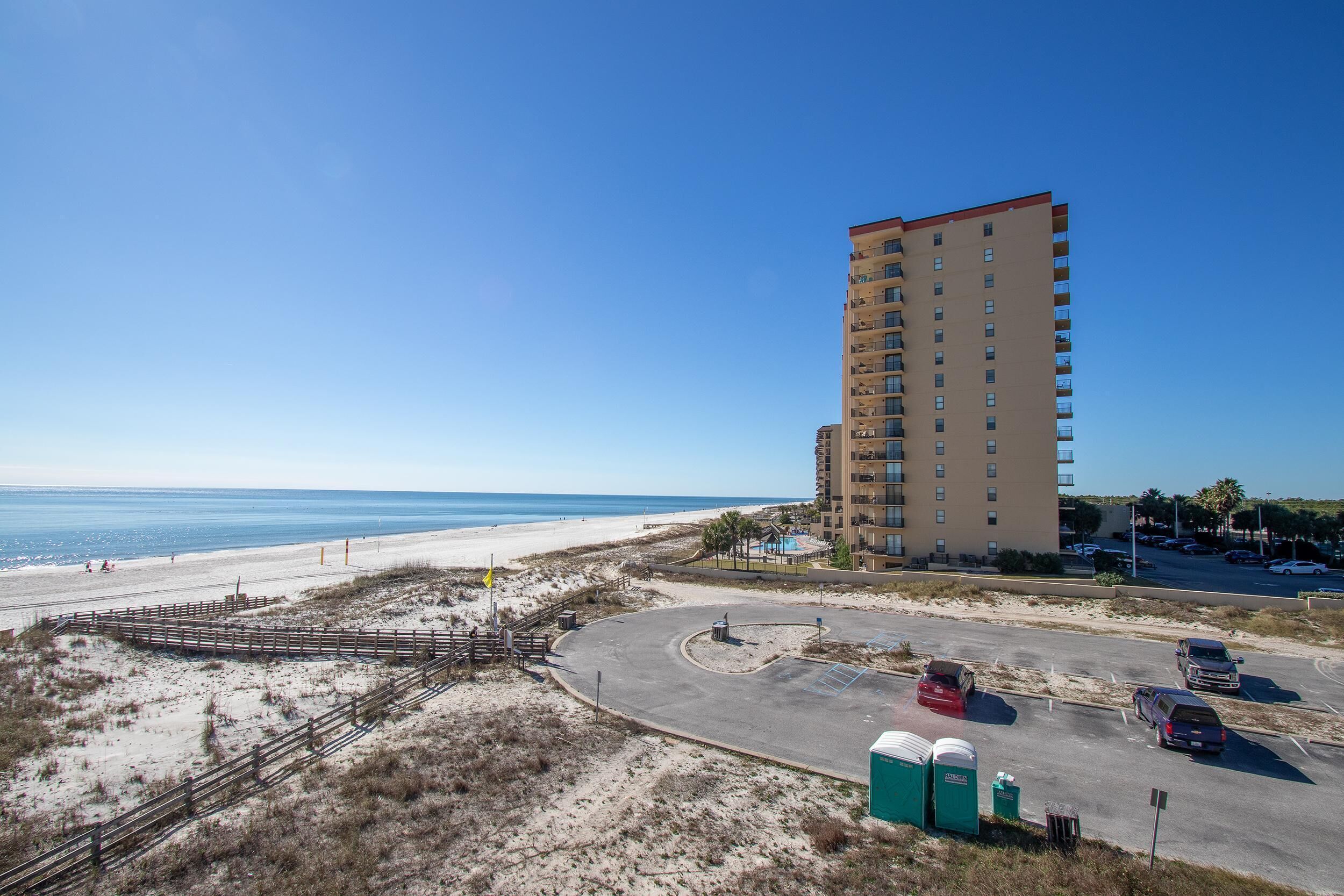 A beachside hotel with a parking lot, a beach, and a clear view of the ocean.