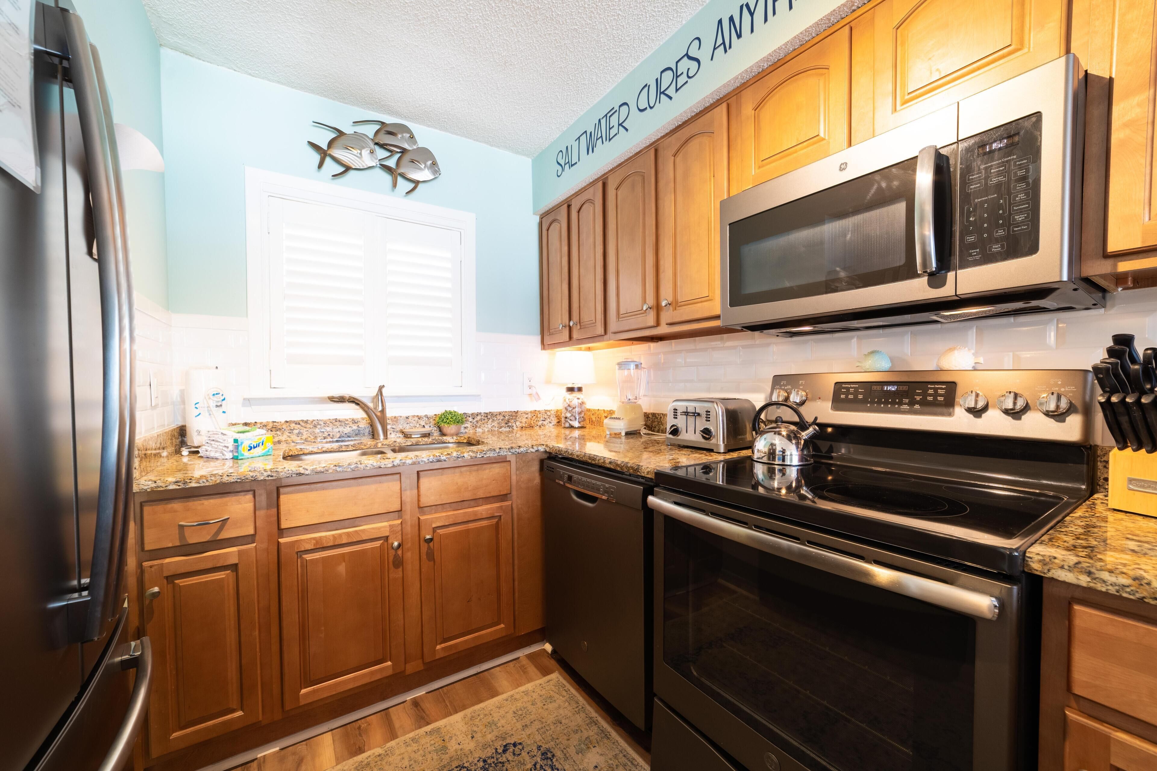 A modern kitchen with wooden cabinets, a stainless steel refrigerator, a microwave, a stove, and a dishwasher.