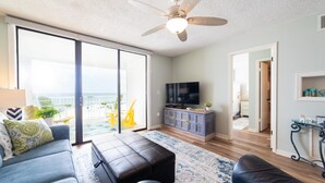 A modern living room with a large sliding glass door leading to a balcony, a ceiling fan, a flat-screen TV, and a wooden cabinet. - Seaside Beach & Racquet 3504 (Orange Beach)