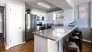 A modern kitchen with a central island, stainless steel appliances, and a view to the dining area. - Seaside Beach & Racquet 4412 (Orange Beach)