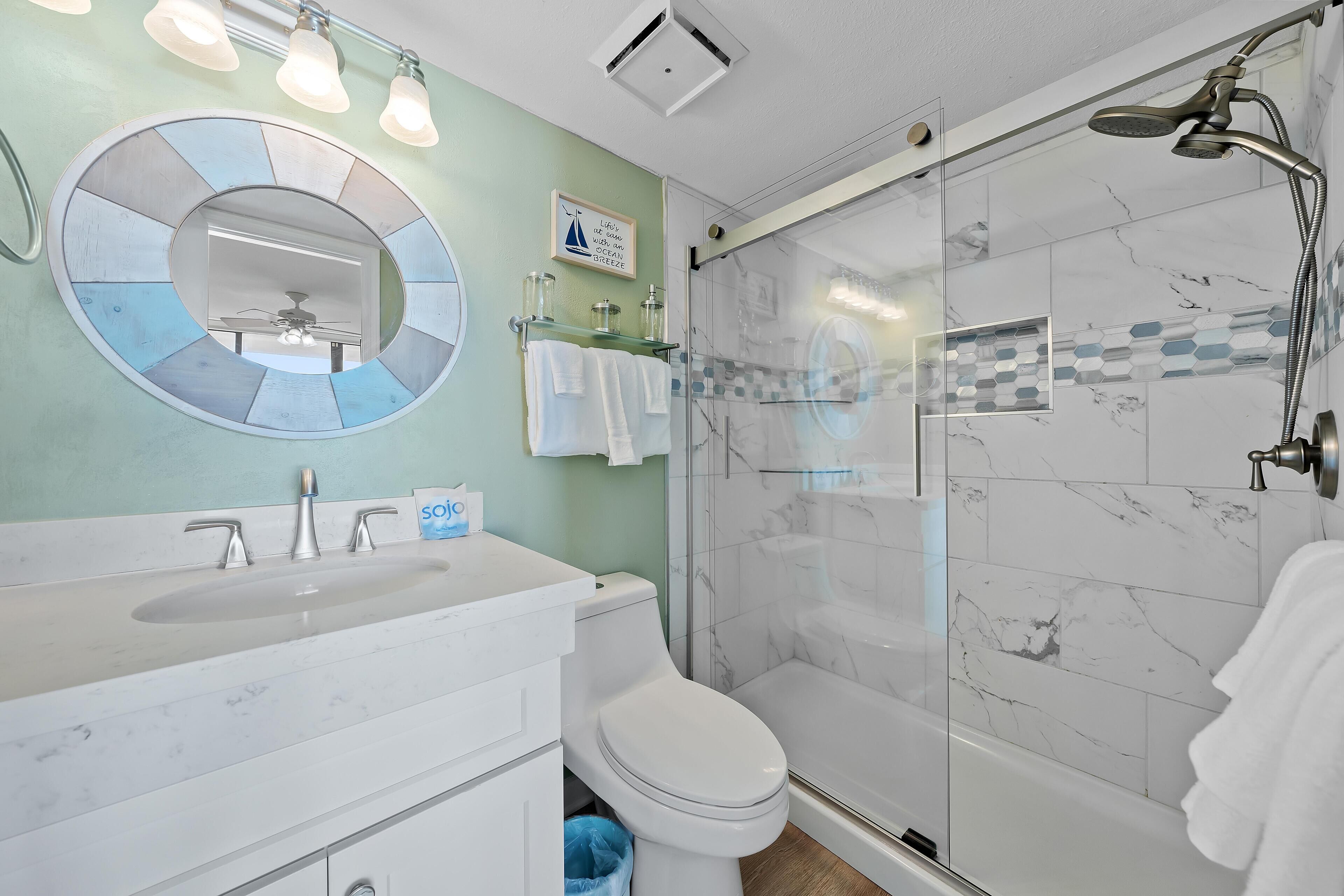 A bathroom with a shower, toilet, sink, and a mirror with a circular design.