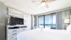 A hotel room with a large bed, a ceiling fan, a flat-screen TV, a dresser, and a view of the ocean. - Seaside Beach & Racquet 4708 (Orange Beach)