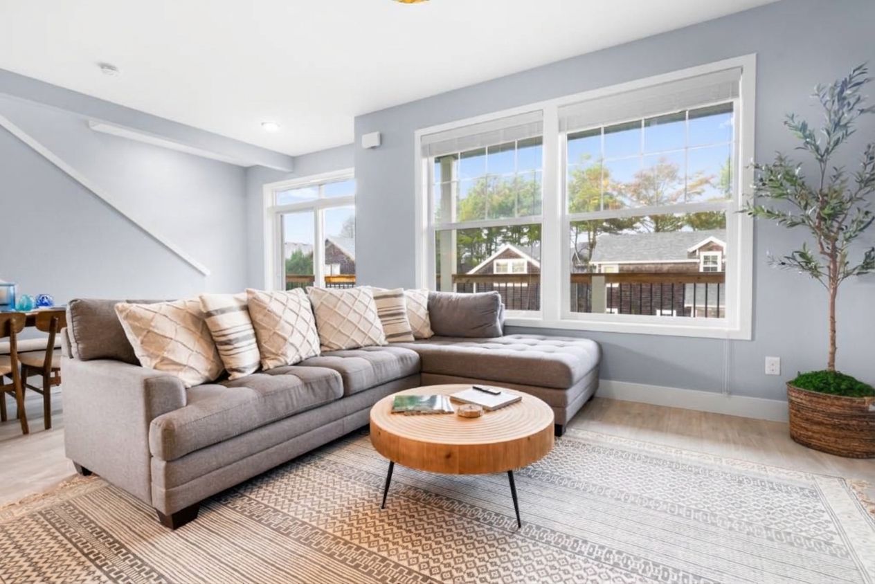 A modern living room with a sectional sofa, a round coffee table, and large windows offering a view of the outside.