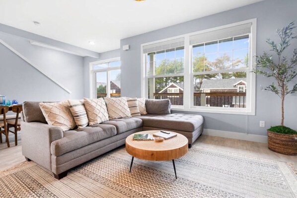A modern living room with a sectional sofa, a round coffee table, and large windows offering a view of the outside.