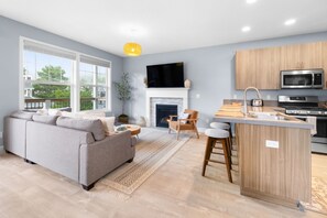 A modern living room with a sofa, a fireplace, a kitchen with a microwave, and a large window.