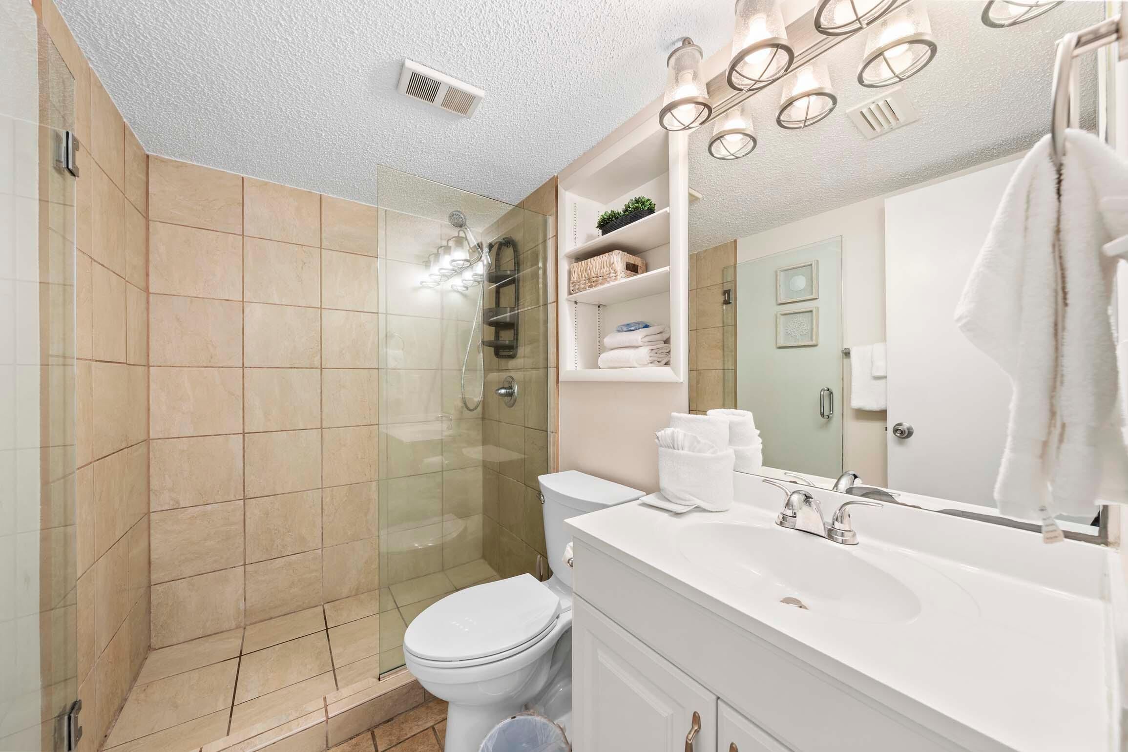 A modern bathroom with a glass shower enclosure, a white toilet, and a vanity with a large mirror and shelves.