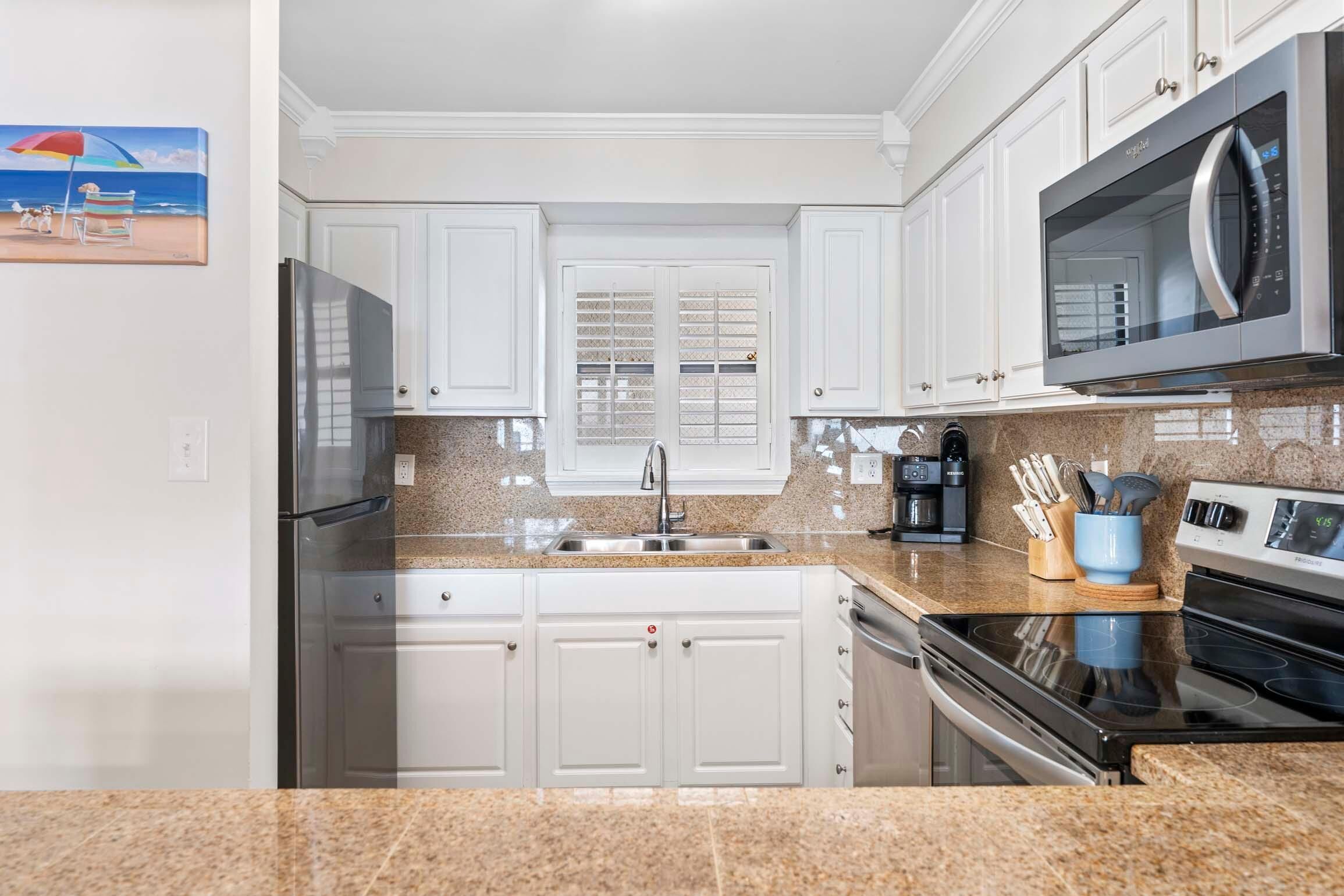 A kitchen with white cabinets, a stainless steel refrigerator, a microwave, and an oven.