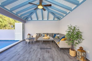 A covered patio with a ceiling fan, seating area, and a view of a swimming pool.