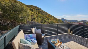 Terraza en la azotea con mobiliario exterior, una mesa con comida y bebidas, y una vista panorámica de una ladera boscosa.
