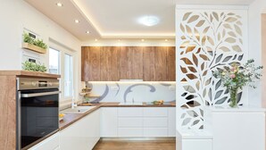 Una cocina moderna con armarios blancos, detalles de madera y un panel decorativo blanco con diseños de hojas.