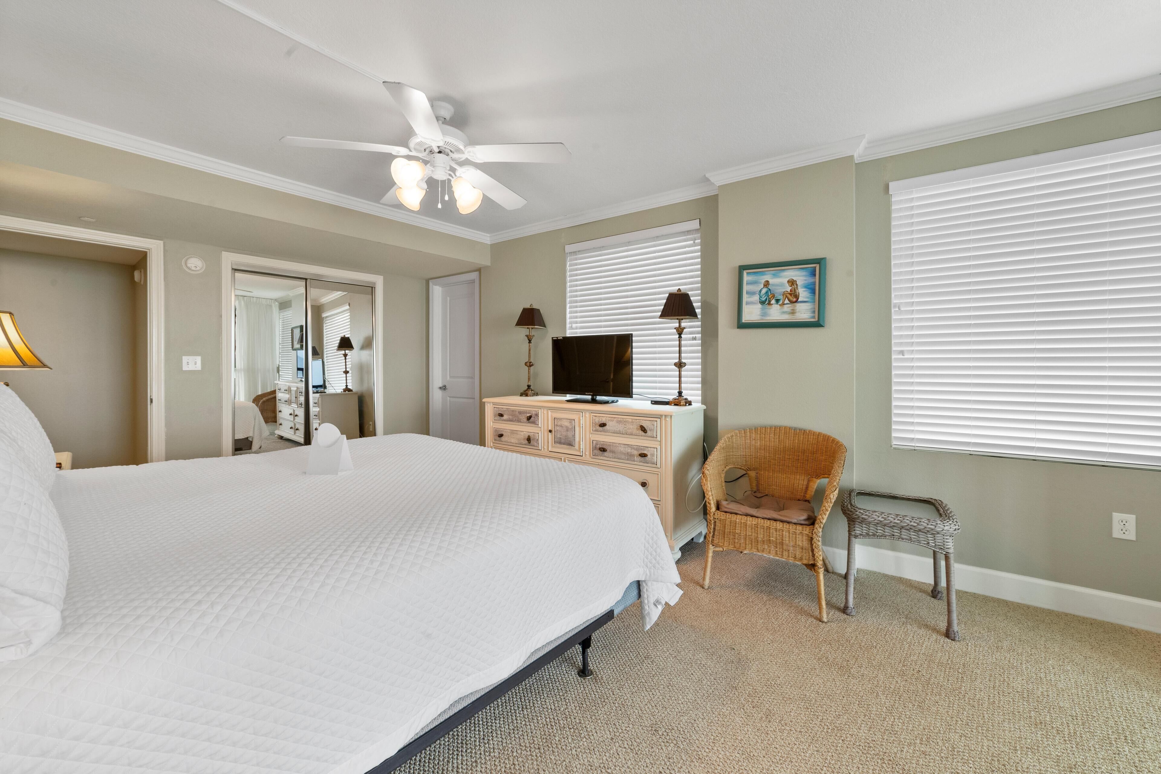 A bedroom with a large bed, a dresser, a television, a chair, and a ceiling fan.