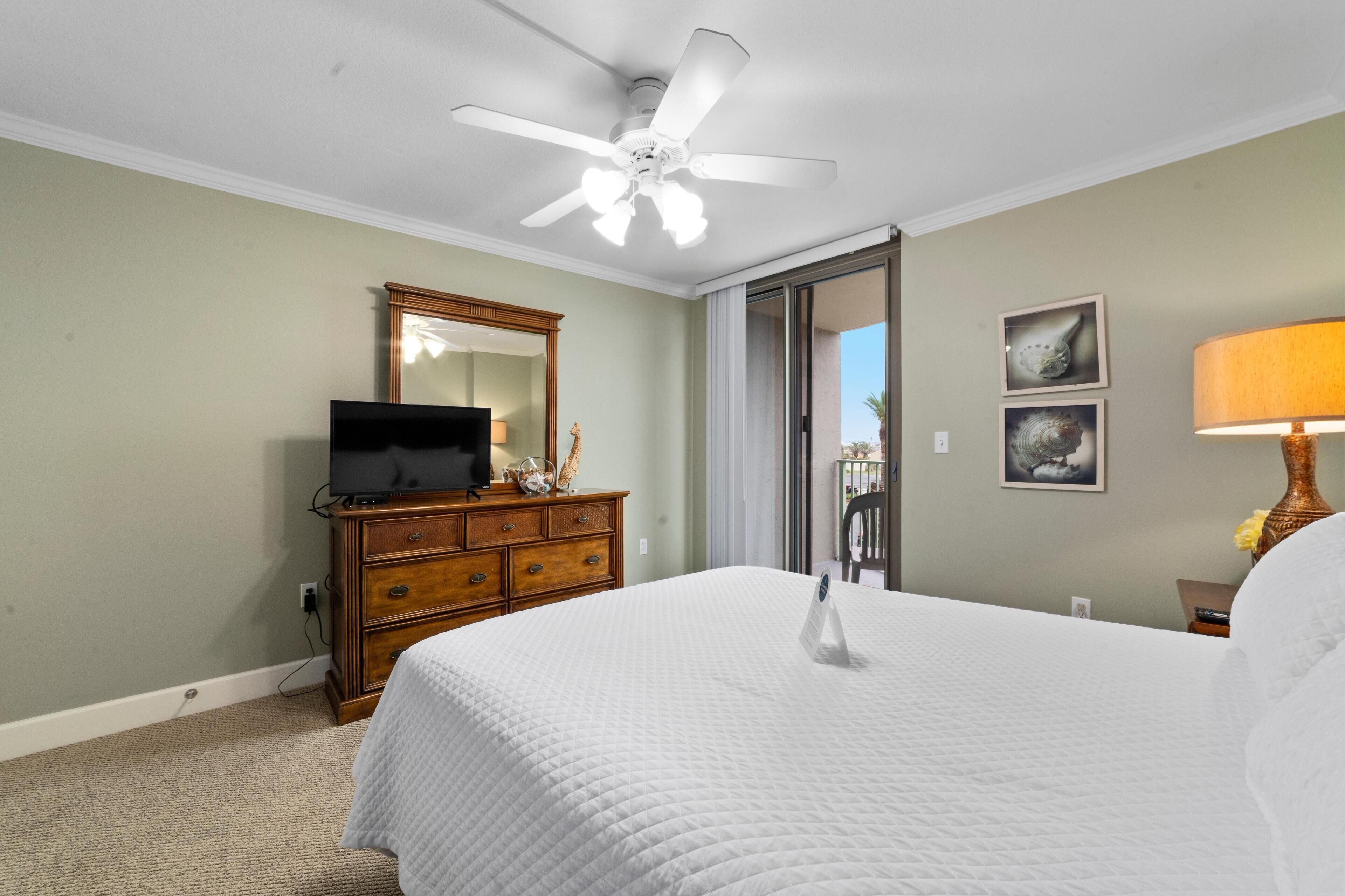 A hotel room with a bed, a dresser, a television, a ceiling fan, and a window with a view.