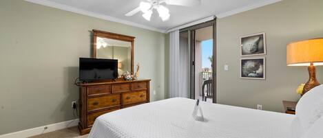 A hotel room with a bed, a dresser, a television, a ceiling fan, and a window with a view.