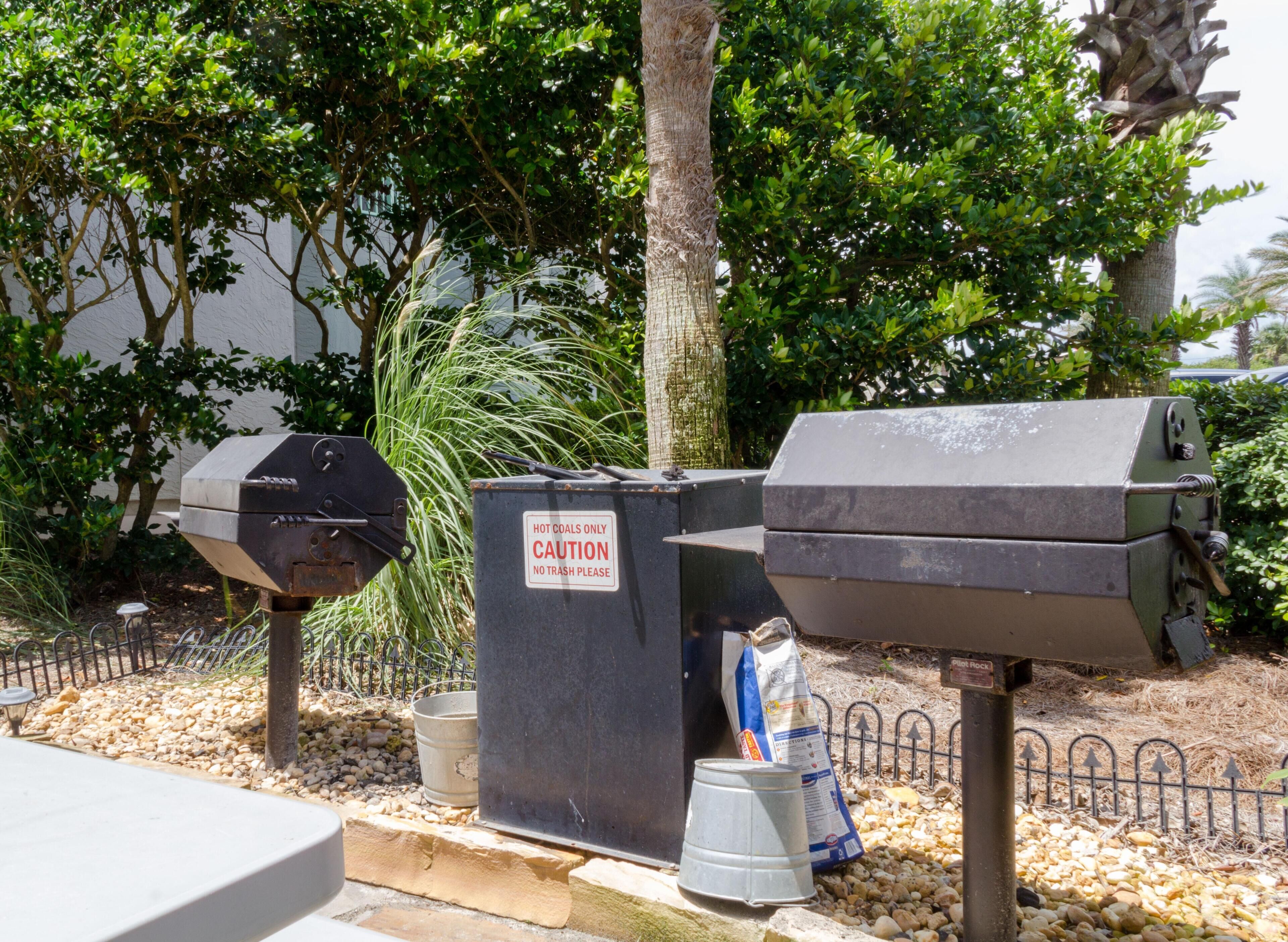 Außenstehende Grillanlagen, ein Warnschild und eine Tüte Holzkohle.