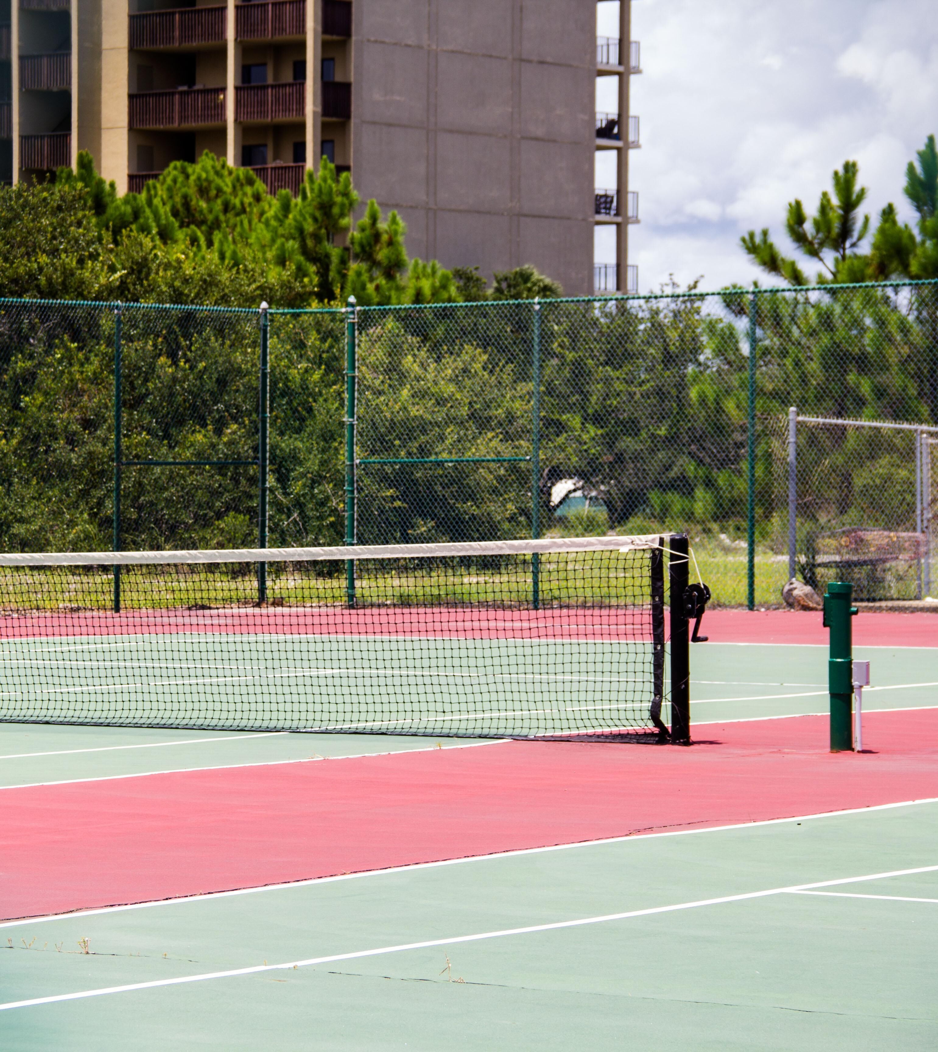 A tennis court with a net, surrounded by a green fence and trees.