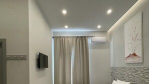 A modern hotel room with a large bed, a flat-screen TV, an air conditioning unit, and a window with curtains. - Naptown Rooms (Naples)