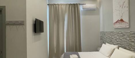 Una habitación de hotel moderna con una cama grande, televisor de pantalla plana, aire acondicionado y una ventana con cortinas.