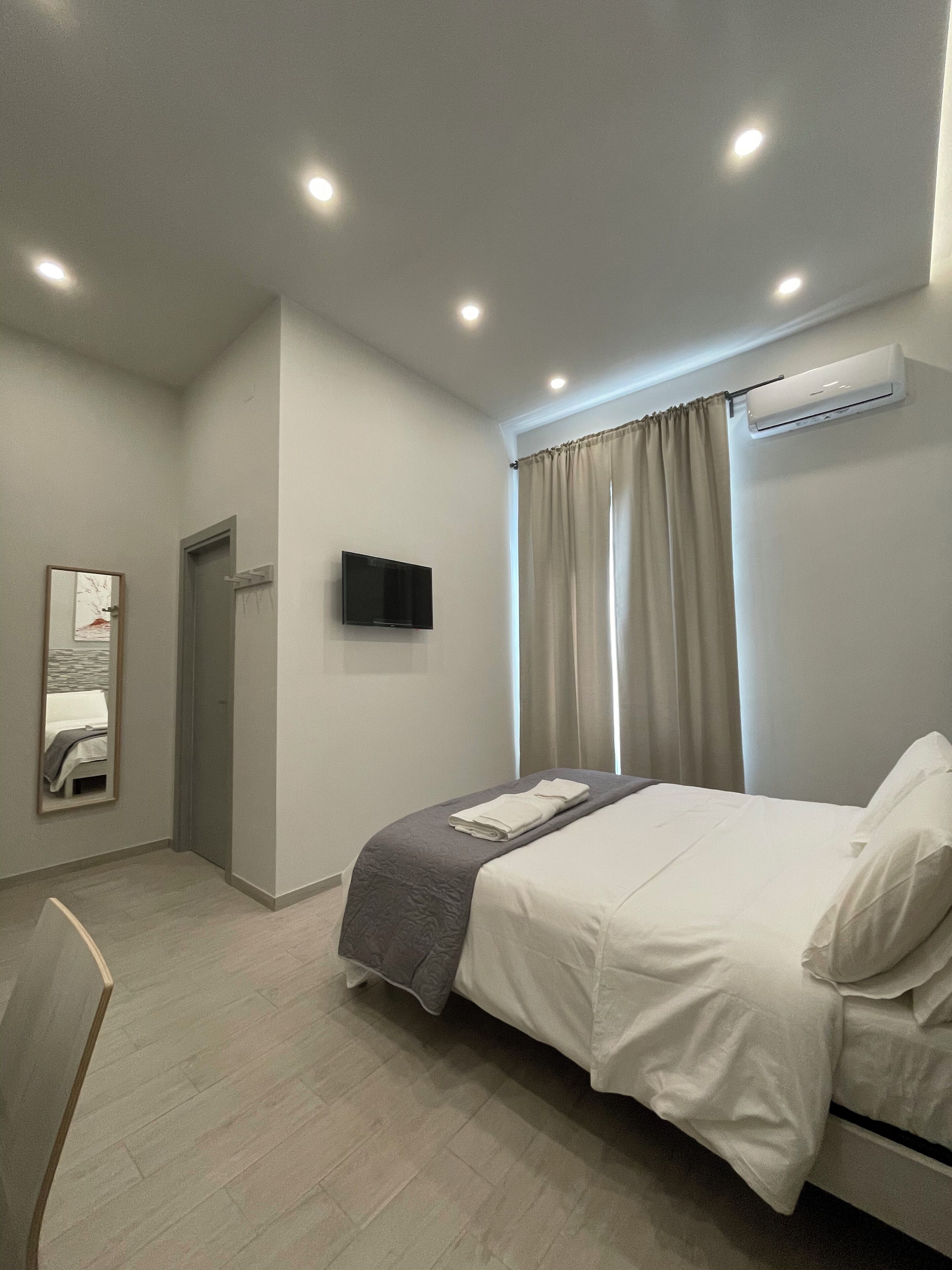 Een moderne hotelkamer met een bed, een flatscreen televisie, een airconditioning en een spiegel.
