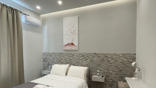 A modern bedroom with a bed, bedside table, desk, and chair. - Naptown Rooms (Naples)