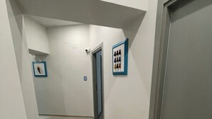 A narrow hallway with a door at the end, a light switch, and a framed picture on the wall. - Naptown Rooms (Naples)