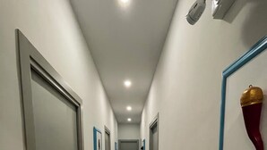 A hallway with doors on both sides, a tiled floor, and a ceiling light. - Naptown Rooms (Naples)
