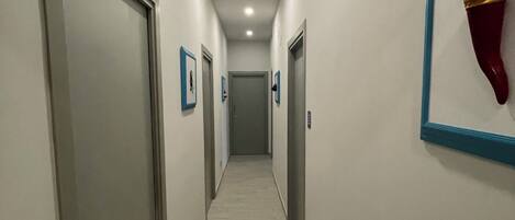 Un couloir avec des portes de chaque côté, un sol carrelé et un luminaire au plafond.