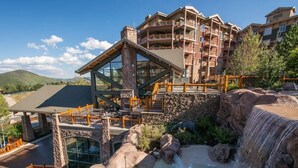 Un hotel con una amplia piscina exterior, una cascada y vistas a la montaña.
