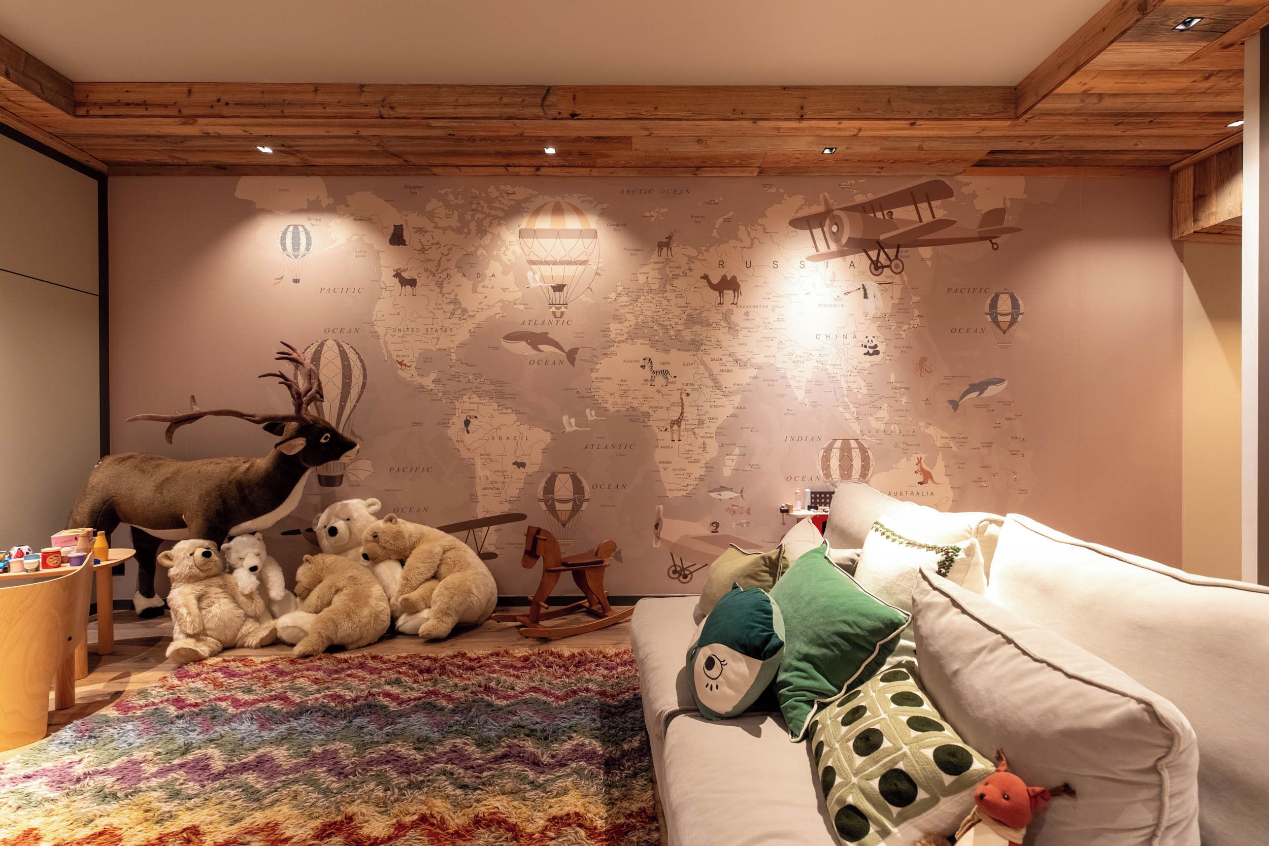 A cozy room with a world map mural, a wooden ceiling, a white sofa with colorful pillows, and a plush toy.