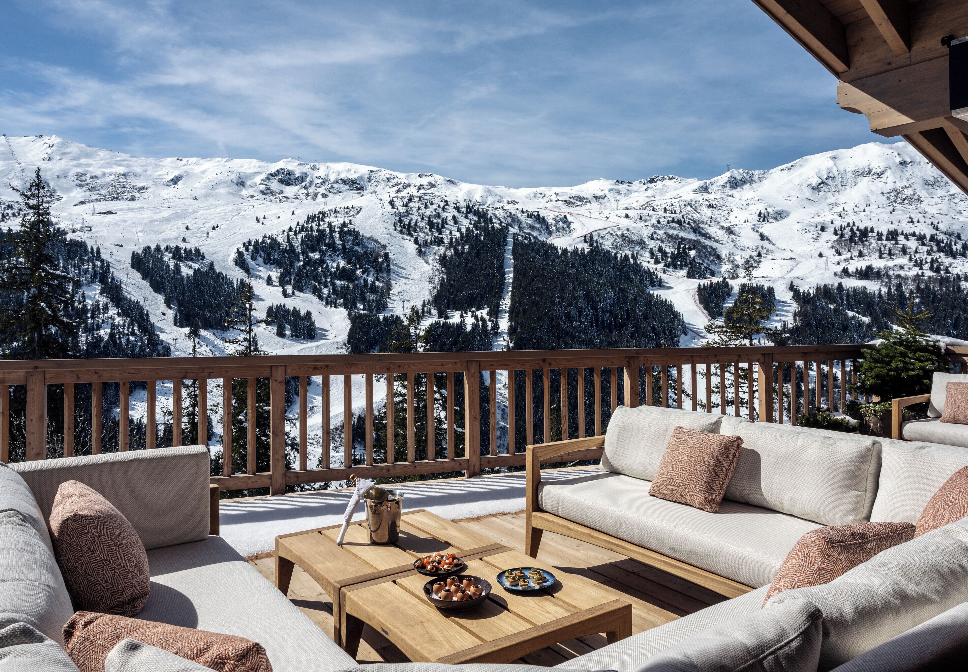 Terraza de madera con sofá y mesa, con vista a un paisaje montañoso nevado.