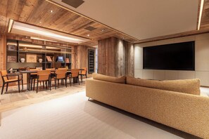 A modern living room with a large flat-screen TV mounted on the wall, a sofa, and a dining area with chairs and a table. - Antares Chalet LUNA ski-in ski-out (Les Allues)
