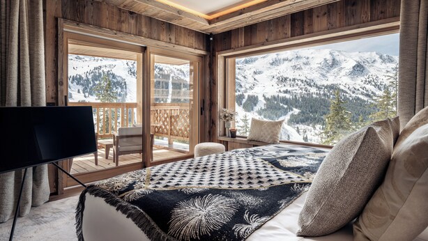 Un dormitorio con un ventanal que ofrece vistas a la montaña, techo de madera y cama con manta estampada.
