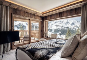 A bedroom with a large window offering a mountain view, a wooden ceiling, and a bed with a patterned blanket.