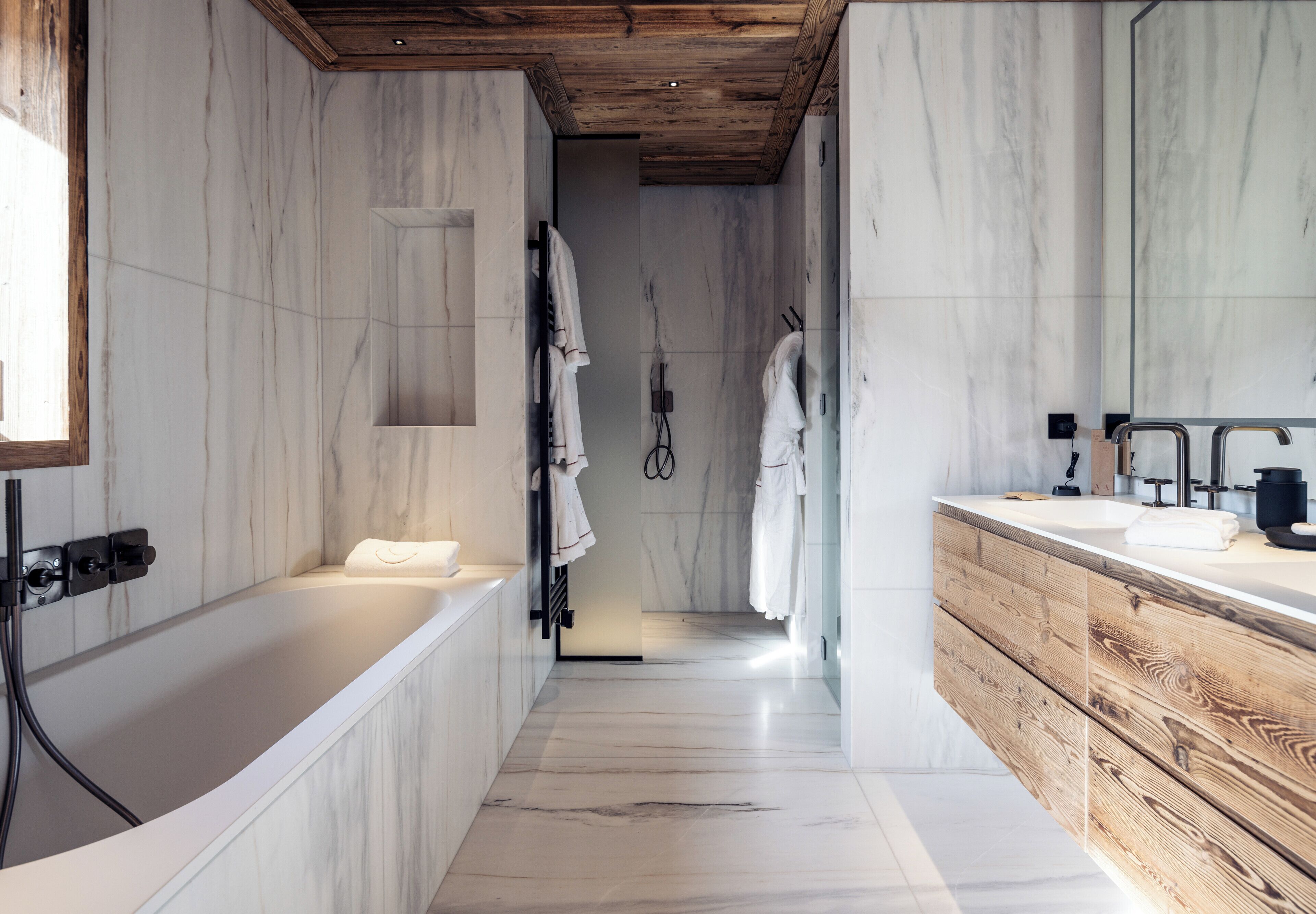 A modern bathroom with a wooden ceiling, marble walls, a freestanding bathtub, and a wooden vanity with a mirror.