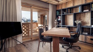 Una habitación moderna con una mesa de madera, dos sillas negras, una estantería y un televisor.
