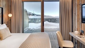 A bedroom with a large bed, a desk, and a view of a snowy landscape through a glass door.