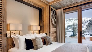 Un dormitorio con una cama grande, cabecera de madera, dos lámparas de noche y vistas a un paisaje montañoso nevado.